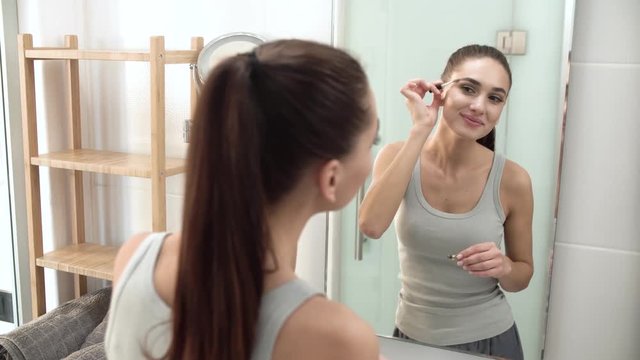 Beauty Makeup. Woman Brushing Eyebrows At Bathroom Mirror