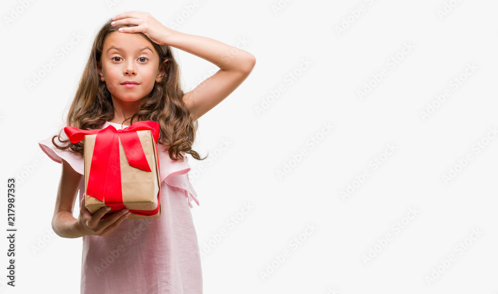 Poster brunette hispanic girl holding a gift stressed with hand on head, shocked with shame and surprise fa