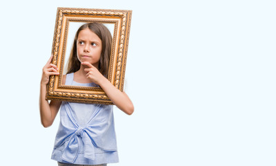 Fototapeta premium Brunette hispanic girl holding vintage art frame serious face thinking about question, very confused idea