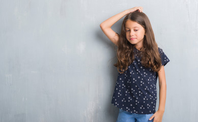 Young hispanic kid over grunge grey wall confuse and wonder about question. Uncertain with doubt, thinking with hand on head. Pensive concept.