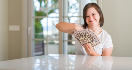 Down syndrome woman at home holding dollars with surprise face pointing finger to himself