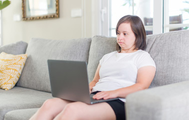 Down syndrome woman at home using computer laptop with a confident expression on smart face thinking serious
