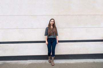 Causal young brunette woman with big building wall behind her