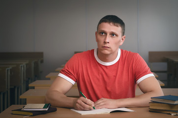 Serious student boy listening a lecture by sitting by school desk.