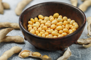 Soybeans in a clay bowl and pods on a gray concrete surface