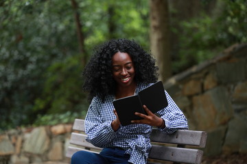 Smiling black woman reading electronic book on bench