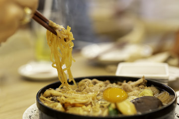 Hand with chopsticks eating Japanese udon noodles with egg.