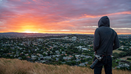 Anonymous man wearing hoody watching sunrise over Auckland city at Mount Eden view point in Auckland, North Island, New Zealand. Travel concepts