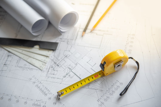 Yellow tape measure (measuring tape), scale and pencils on architectural drawing plan of house project, blueprint rolls on working table, Architecture drawing tools and building construction concepts