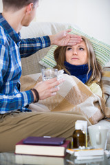  woman with cold lying on couch, boyfriend taking care