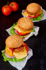 Three tasty burgers with falafel, salad, onion rings, cheese, tomatoes and chili pepper on the black background. Classic american veggie fast food. Side view