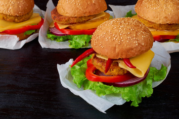 Homemade tasty burger with falafel, salad, onion rings, cheese, tomatoes and chili pepper on the black background. Classic american veggie fast food. Close up view