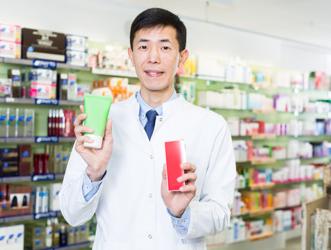 Positive chinese man pharmacist is standing with medicines