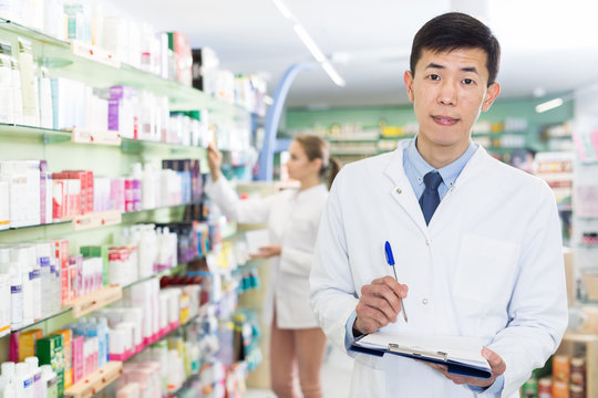 Chinese male is attentively looking medicine with notebook in apothecary