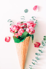 Creative minimalist composition with waffle cone with pink roses and eucalyptus inside on white background.