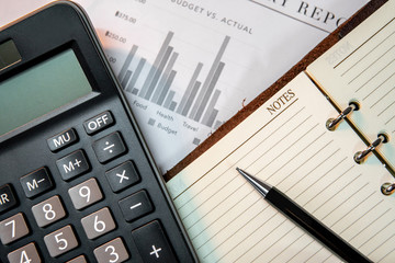 Calculator, pen, blank lined paper page of notebook and summary report paperwork with bar graph and table. Financial data analysis. Business planning and management concept