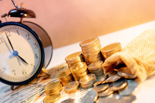 Clock with banknotes and coin stack of international currency on table. Time investment or retirement saving. Business and finance concepts