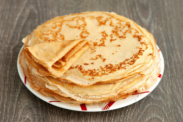 A stack of thin pancakes on a wooden background. Maslenitsa. Pancakes on a saucer close-up. Dessert for breakfast in the form of pancakes.