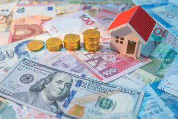 Real estate or property investment. Home mortgage loan rate. Saving money for retirement concept. Coin stack on various of international banknotes with house model on table. Business growth concept.