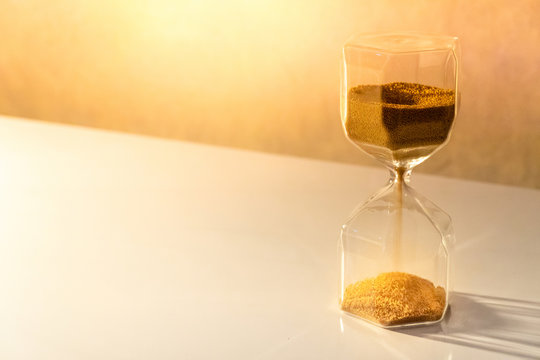Gold sand running through the shape of modern hourglass on white table.Time passing and running out of time. Urgency countdown timer for business deadline concept