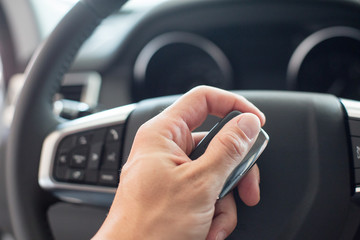 Male hand holding a car key and steering wheel