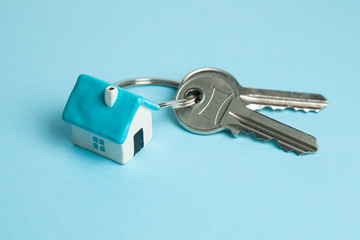 Keys and a keychain house on a blue background. Concept of buying a house