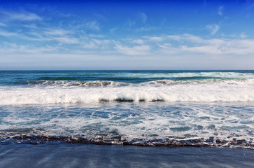 Big breaking Ocean wave on a black sandy beach on Pacific ocean