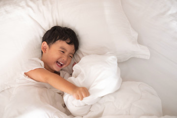 3 years old little cute Asian boy at home on the bed, kid lying playing and smiling on white bed with pillow and blanket, top view with copy space.