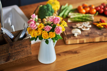 Beautiful bouquet of multicolored roses in white vase on the kitchen table.