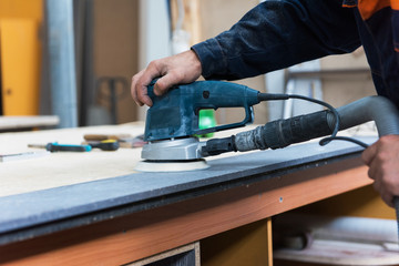 Furniture production or craft concept: worker polishing the stone surface of furniture part with polish machine
