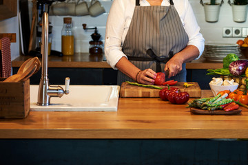 Senior woman hands chopping vegetables on a wooden board in the kitchen.