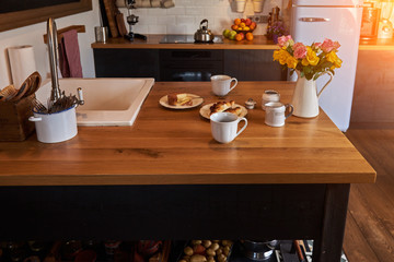 Rural breakfast homemade cheese and croissants with roses bouquet in jug. Kitchen in the attic and rustic style.  Wall with shelves, trays, jars, mugs, sink. In the background a wall of white brick.