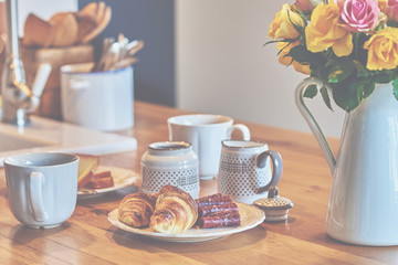 Romantic rural breakfast - milk, croissants and a cups of coffee on rustic brown wood table. Countryside weekend morning concept.