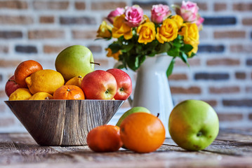 A large bowl of fruit and flowers on brick wall background.