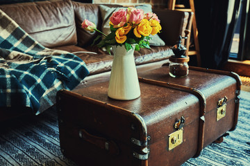 Modern living room interior with leather sofa decorated with a vase of flowers on a vintage coffee table.