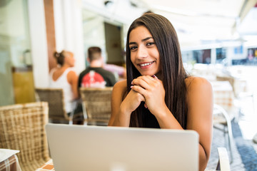 Pretty latin woman student with cute smile keyboarding something on laptop while relaxing after lectures in University. Beautiful happy woman working on laptop computer during coffee break in cafe bar