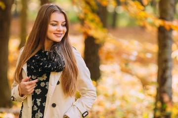 Fototapeta na wymiar Portrait of a beautiful, dreamy and smile girl with long hair in nice white coat and scarf standing in a park in autumn.