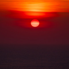 Sunset over ocean horizon photographed with big telephoto lens.