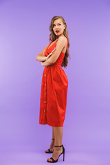 Full length portrait of elegant brunette woman 20s wearing red dress smiling and looking aside, standing isolated over violet background