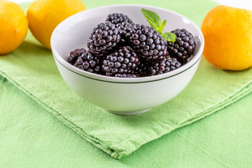 Delicious fresh blackberries and ripe black and reddish garnet. In white bowl on green and white background. With apricots.
