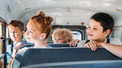 group of schoolchildren riding on school bus and looking through window