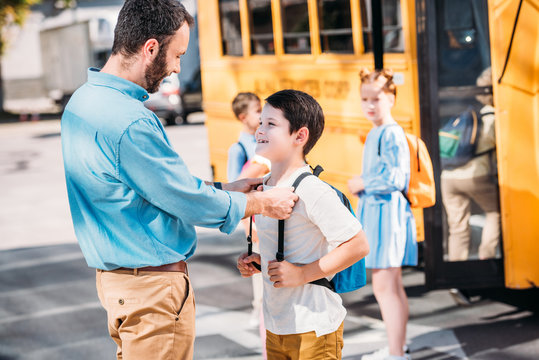 handsome father talking to his son before school in front of school bus with his classmates