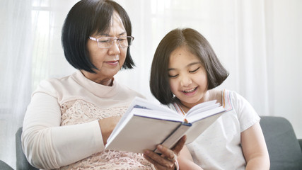Happy Asian grandmother and lovely girl reading book together at home