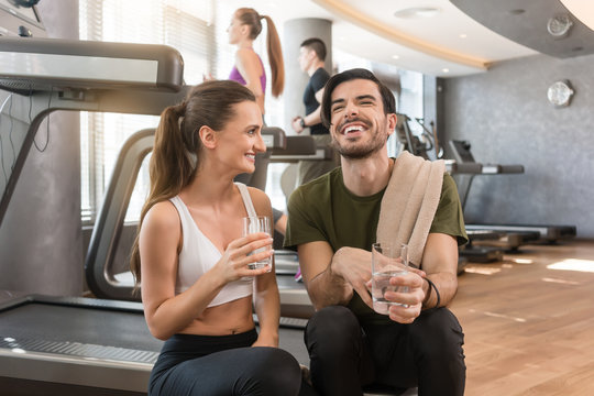 Cheerful young man and woman with a healthy lifestyle drinking plain water for hydration during break at the fitness club