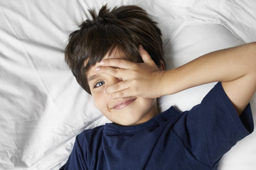 Kid peering through fingers from bed