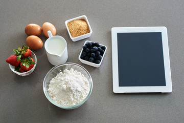 White tablet computer with blank screen with ingredients for baking close up.