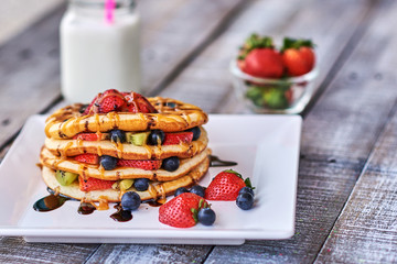 Big Pile of American Pancakes with berries, strawberry, kiwi and Maple Syrup