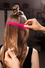 Naklejka premium model with a topknot having her hair being brushed by a professional hairdresser using a pink brush in a beauty salon. concept of carefull hair treating