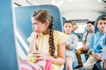 sad little schoolgirl riding on school bus with her classmates
