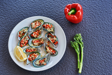 Mussel shells with vegetables and cheese on a white dish. Top view.